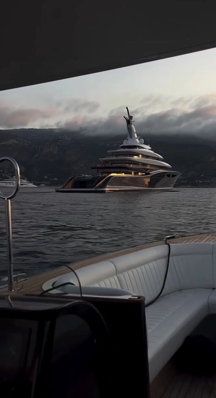 Superyacht at a dusk anchorage below a mountainous coastline